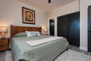 Ein Schlafzimmer mit einem Bett, Nachttischen, einem gerahmten Bild und einer dunklen Tür.