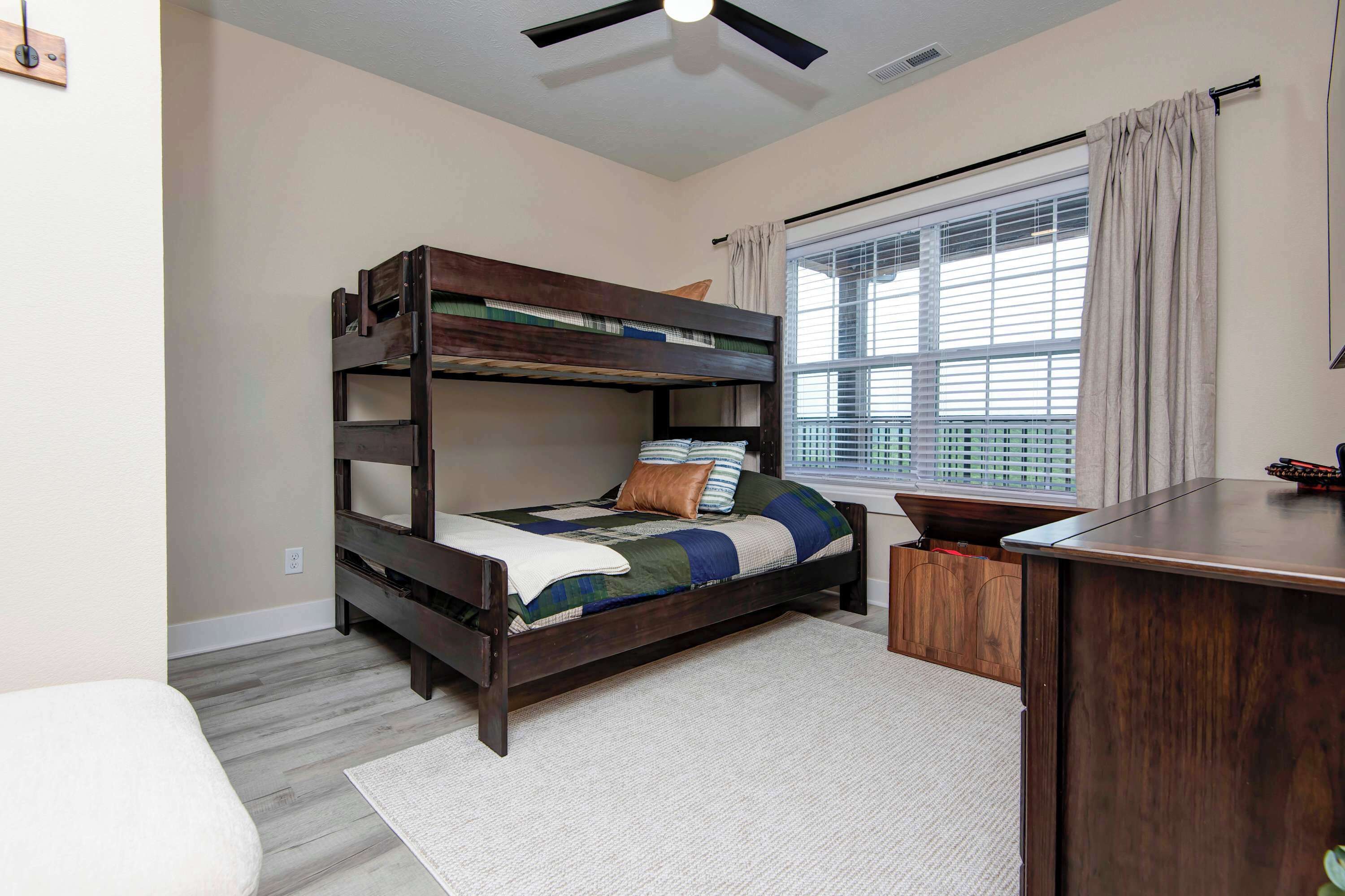 A bunk bed with a desk and a window with blinds.