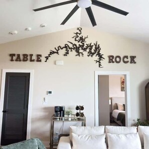 Ein Zimmer mit Deckenventilator, einem Bett, einem Couchtisch und einer Wand, auf der oberhalb einer Zierpflanze der Schriftzug 'TABLE ROCK' steht.