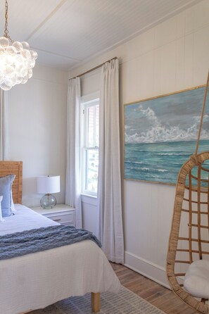 A bedroom with a bed, a hanging chair, a painting of the sea, and a window with curtains. - 3-bedroom professionally designed bungalow in tranquil Vero Beach, Fl. (Vero Beach)