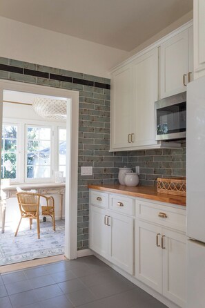 A kitchen with white cabinets, a microwave, and a tiled backsplash. - 3-bedroom professionally designed bungalow in tranquil Vero Beach, Fl. (Vero Beach)