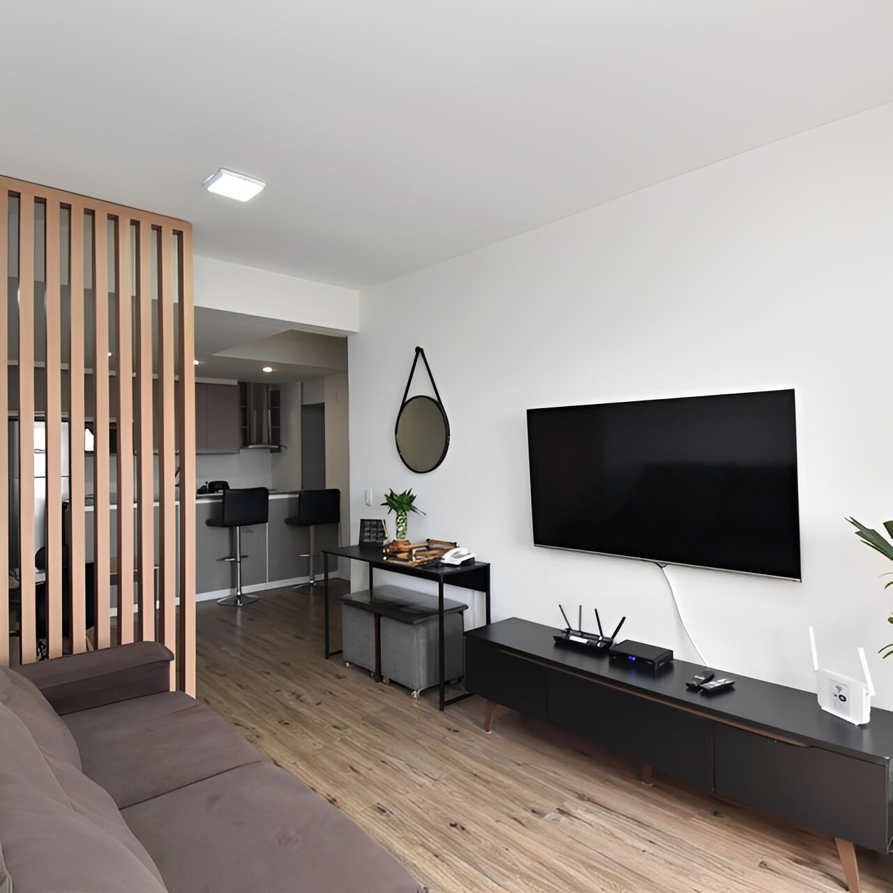 A modern living room with a flat-screen TV, a sofa, a coffee table, and a dining area with a kitchen in the background.