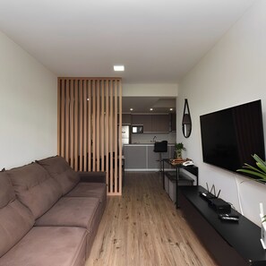 Een moderne woonkamer met een bank, een televisie en een keuken op de achtergrond.