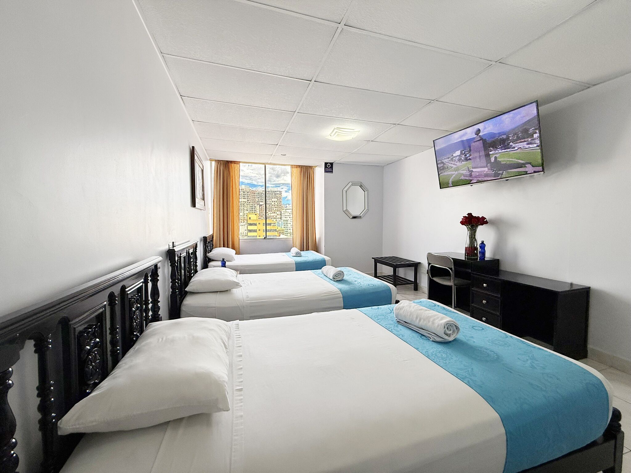 A hotel room with two beds, a desk, a chair, a TV, and a window with a city view.