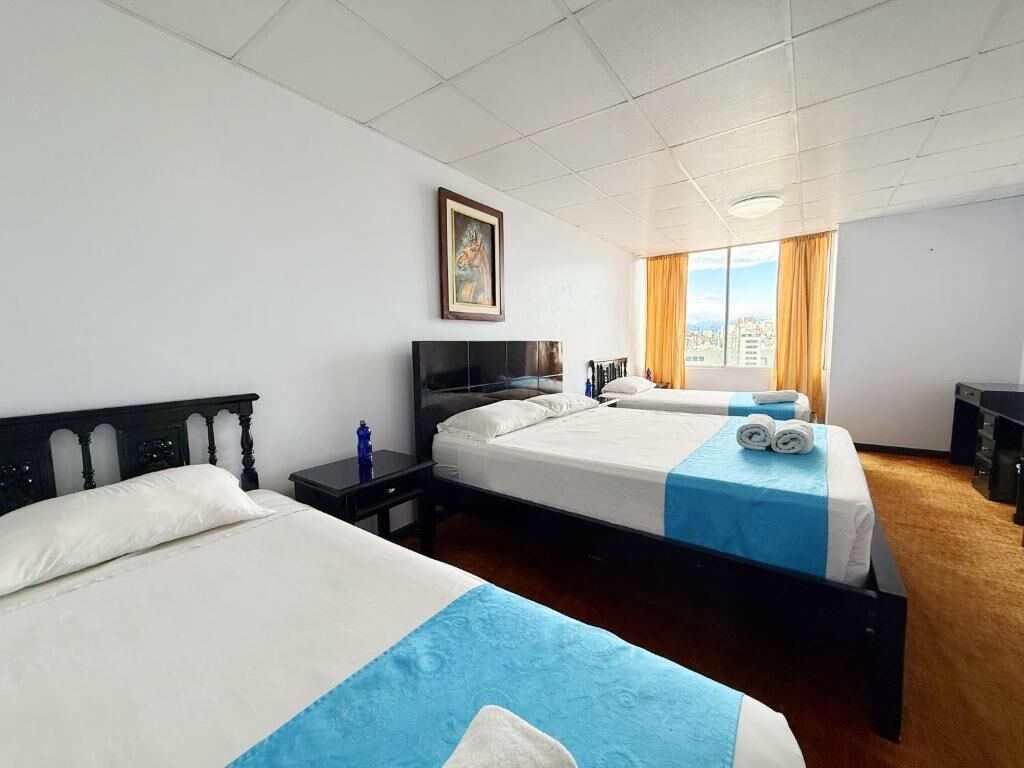 Una camera d'albergo con due letti, un'ampia finestra con tende e un quadro appeso al muro, affacciata sulla città.