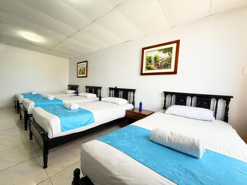 Habitación de hotel con tres camas, un cuadro en la pared y una mesita con una botella.