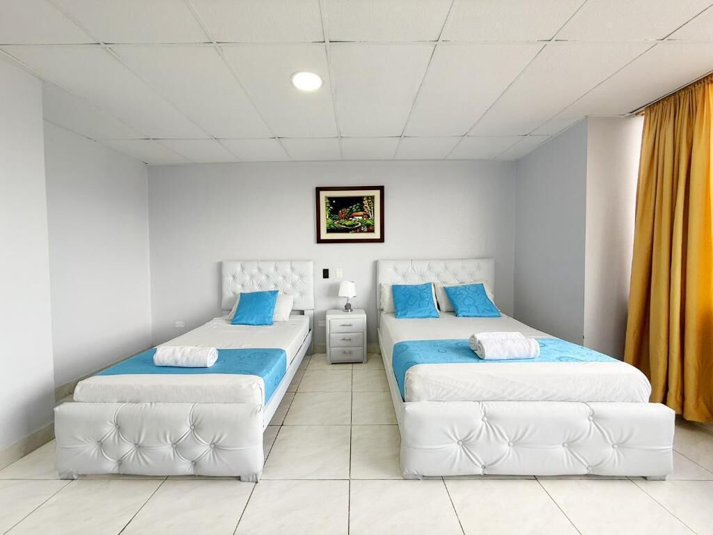 Une chambre d’hôtel avec deux lits, une table de chevet, un tableau encadré au mur et une fenêtre avec des rideaux.
