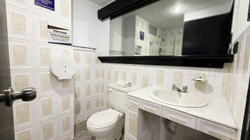 Un baño pequeño con inodoro, lavamanos y espejo. Hay carteles en la pared, uno de los cuales indica "Se requiere el uso de agua".