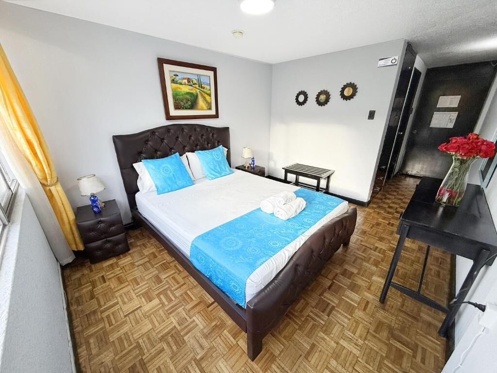 A bedroom with a bed, a bedside table, a nightstand, a wall-mounted picture, and a door.