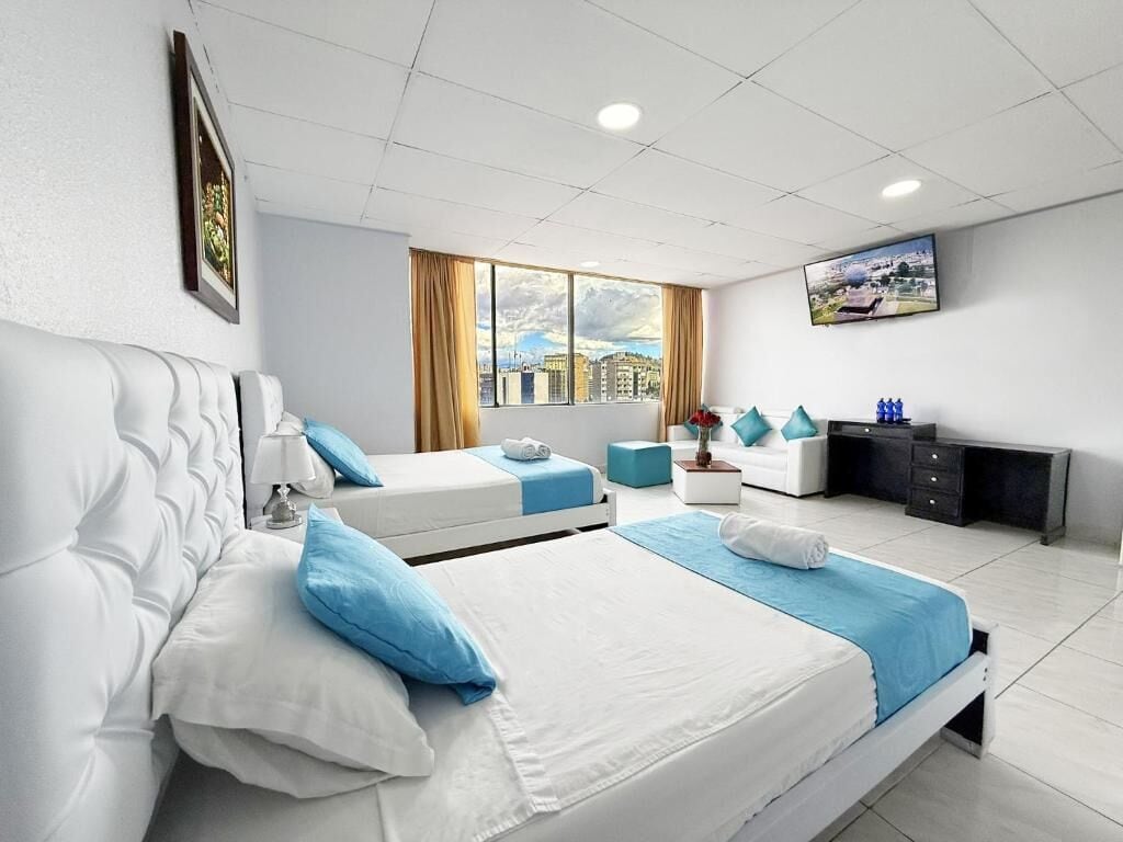 A hotel room with two beds, a TV, a desk, and a window with a city view.