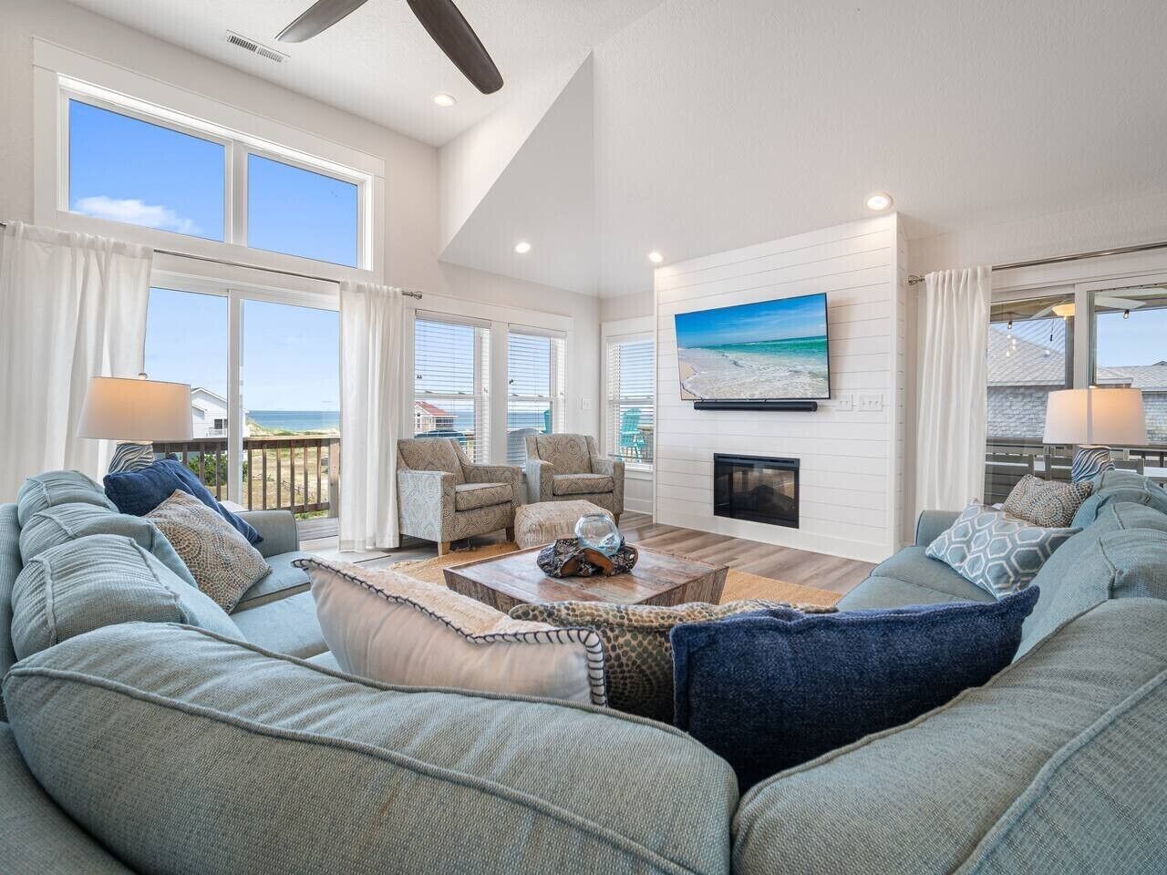 A spacious living room with a large window, a fireplace, and a view of the beach.