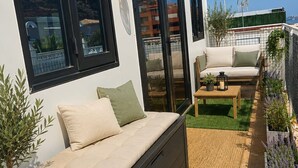 Una zona salotto esterna moderna con divano, tavolino e piante in vaso.
