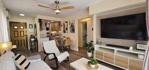 Ein Wohnzimmer mit einer Couch, einem Fernseher, einem Deckenventilator und einem Essbereich mit Stühlen und einem Tisch.