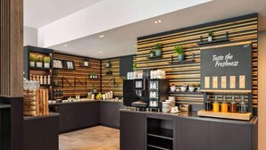 Ein modernes Café-Interieur mit Fischgrat-Holzboden, schwarzer und Holz-Einrichtung und einem Schild mit der Aufschrift 'Taste the Freshness'.
