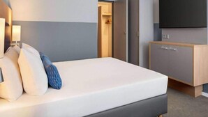 A hotel room with a bed, a TV mounted on the wall, and a wardrobe.