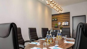 Ein Konferenzraum mit einem runden Tisch, schwarzen Ledersesseln, einer modernen Pendelleuchte und einer Wandablage mit Pflanzen und Dekoration.