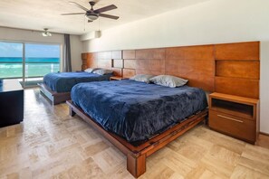 Ein Schlafzimmer mit zwei Betten, einem Holzkopfende, einem Deckenventilator und einem großen Fenster mit Meerblick.