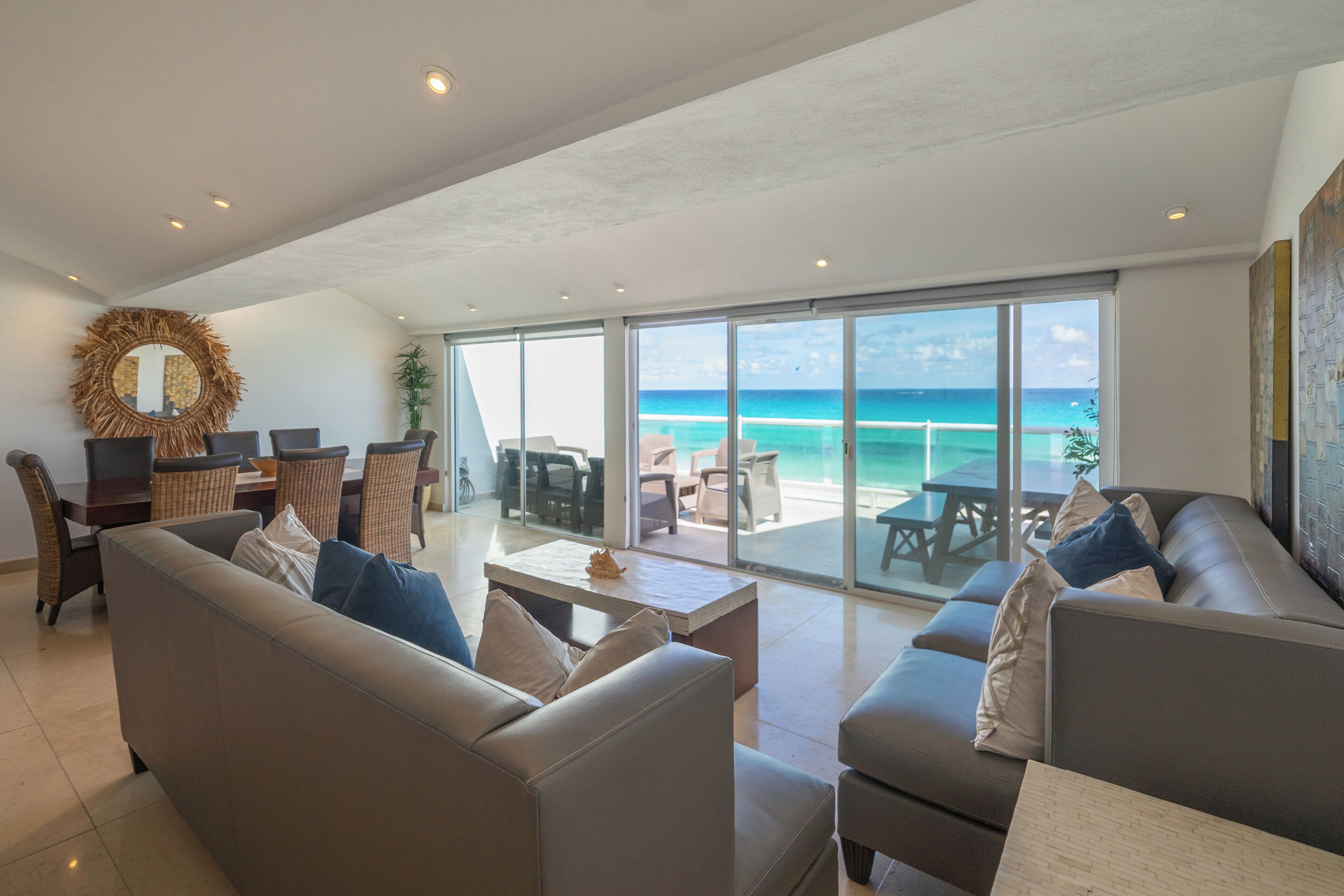 A spacious living area with a large window overlooking a beach. There are multiple seating arrangements including sofas and chairs.