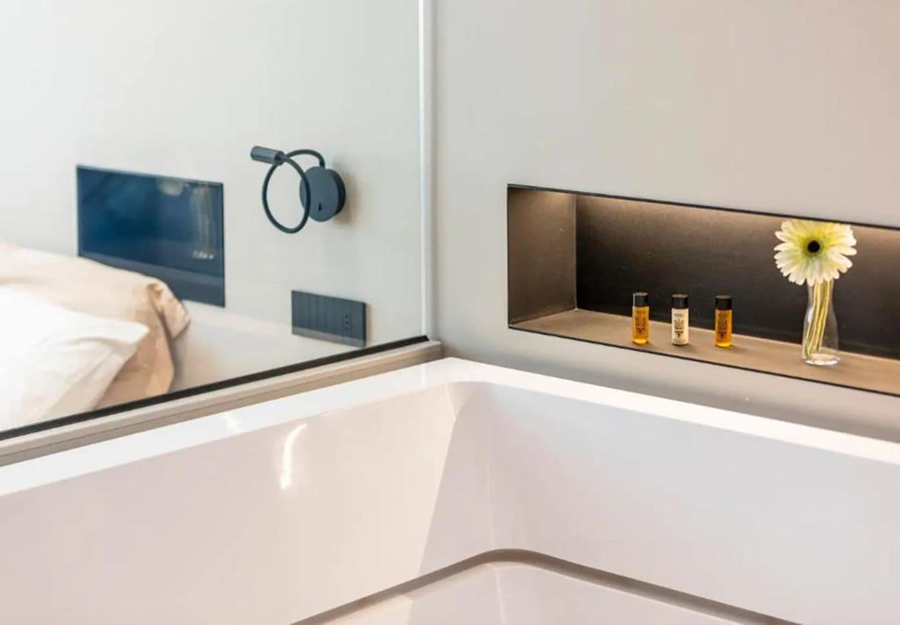 Ein modernes Hotelzimmer mit einem Bett, einem Nachttisch mit einer Vase und Kerzen sowie einem an der Wand montierten Lautsprecher.