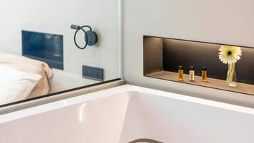 Ein modernes Hotelzimmer mit einem Bett, einem Nachttisch mit einer Vase und Kerzen sowie einem an der Wand montierten Lautsprecher.