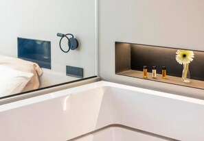 A modern hotel room with a bed, a bedside table with a vase and candles, and a wall-mounted speaker. - Zoe luxury suites (Catania)
