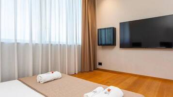 Ein Hotelzimmer mit Bett, zwei zusammengerollten Handtüchern, einem Flachbildfernseher und einem Fenster mit Vorhängen.