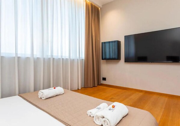 A hotel room with a bed, two rolled towels, a flat-screen TV, and a window with curtains. - Zoe luxury suites (Catania)