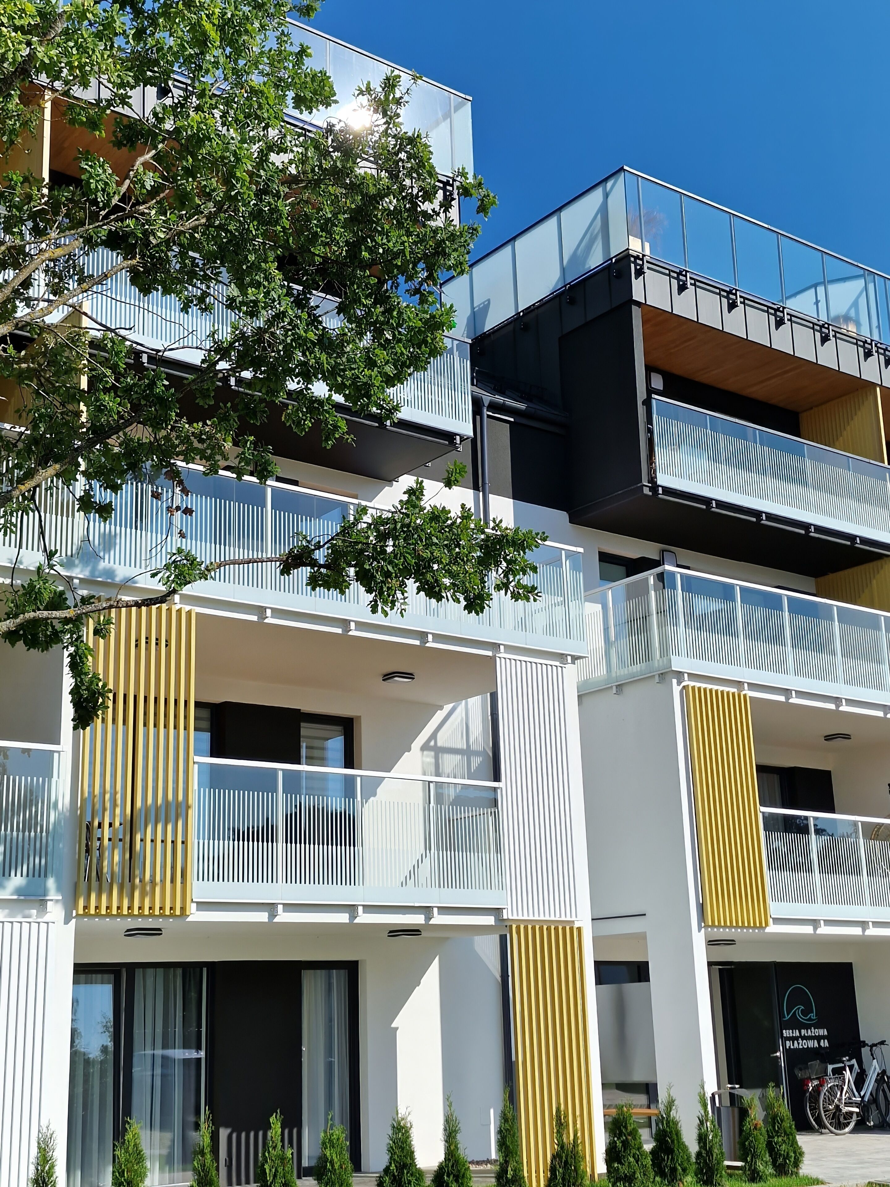 Un immeuble à plusieurs étages doté de balcons, un arbre au premier plan et un ciel bleu dégagé.