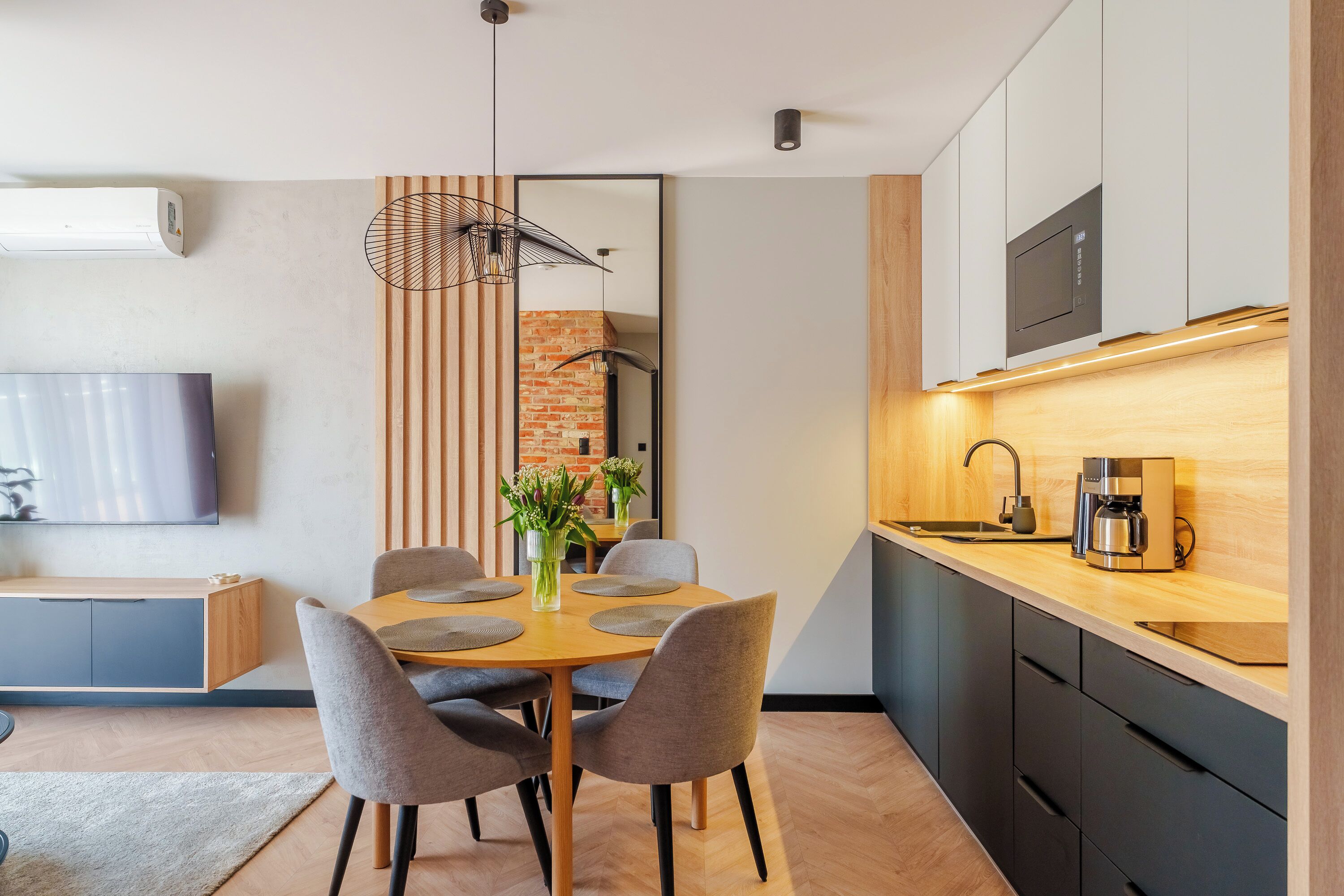 A modern kitchen with a dining area, a flat-screen TV, and a coffee maker.