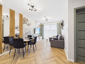 A modern living room with a dining area, a sofa, a TV, and a wooden floor. - Posesja Plażowa 4c I & SPA (Grzybowo)