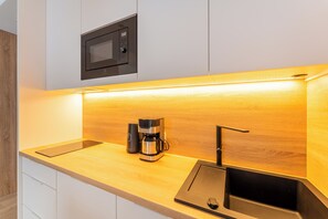 Una cocina moderna con microondas integrado, cafetera y un elegante lavamanos negro.