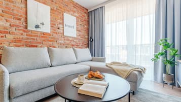 Ein modernes Wohnzimmer mit Backsteinwand, einer Couch, einem Couchtisch mit einem Buch und Croissants sowie einer Pflanze.