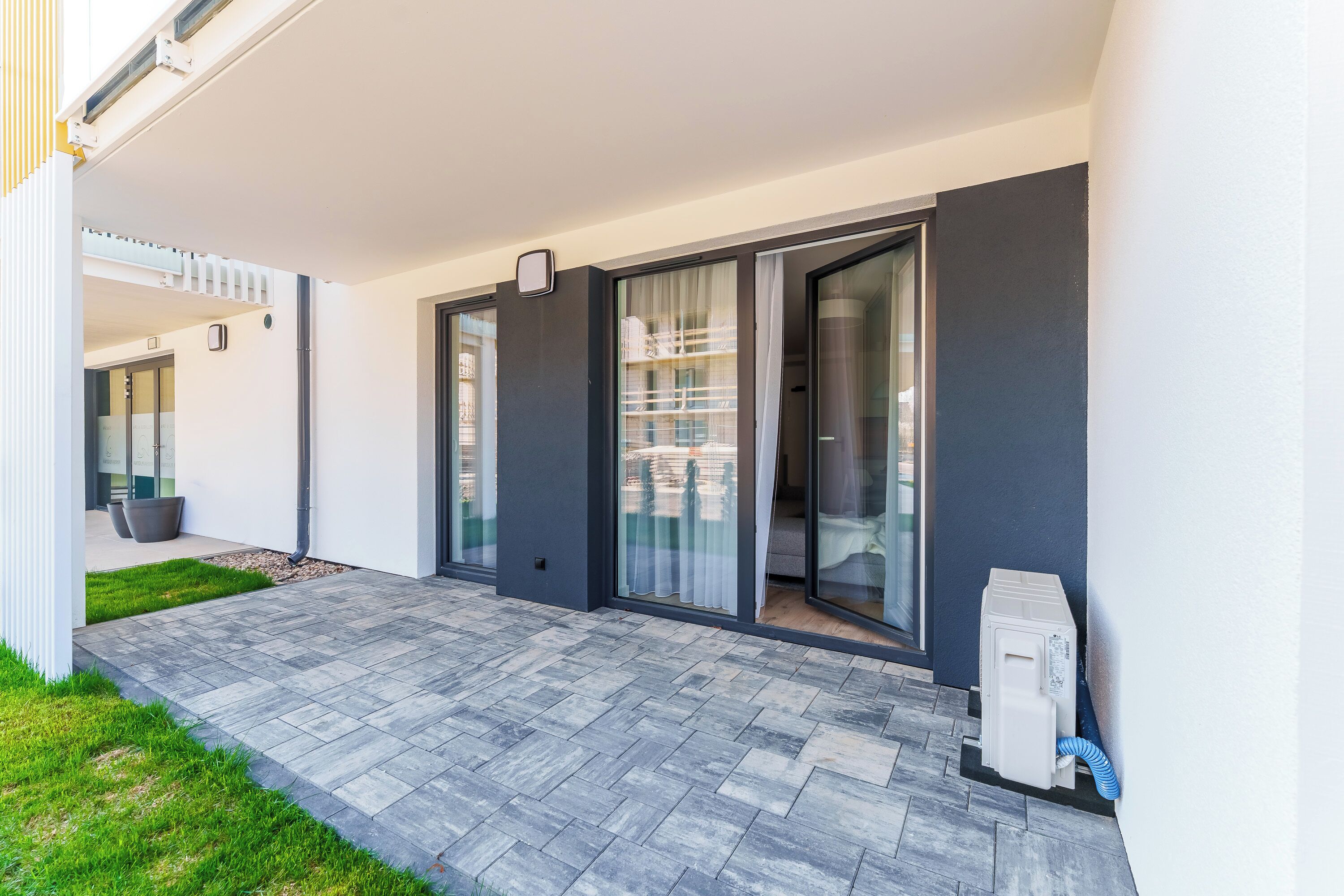 A modern building with a patio area, large sliding glass doors, and a small outdoor heater.
