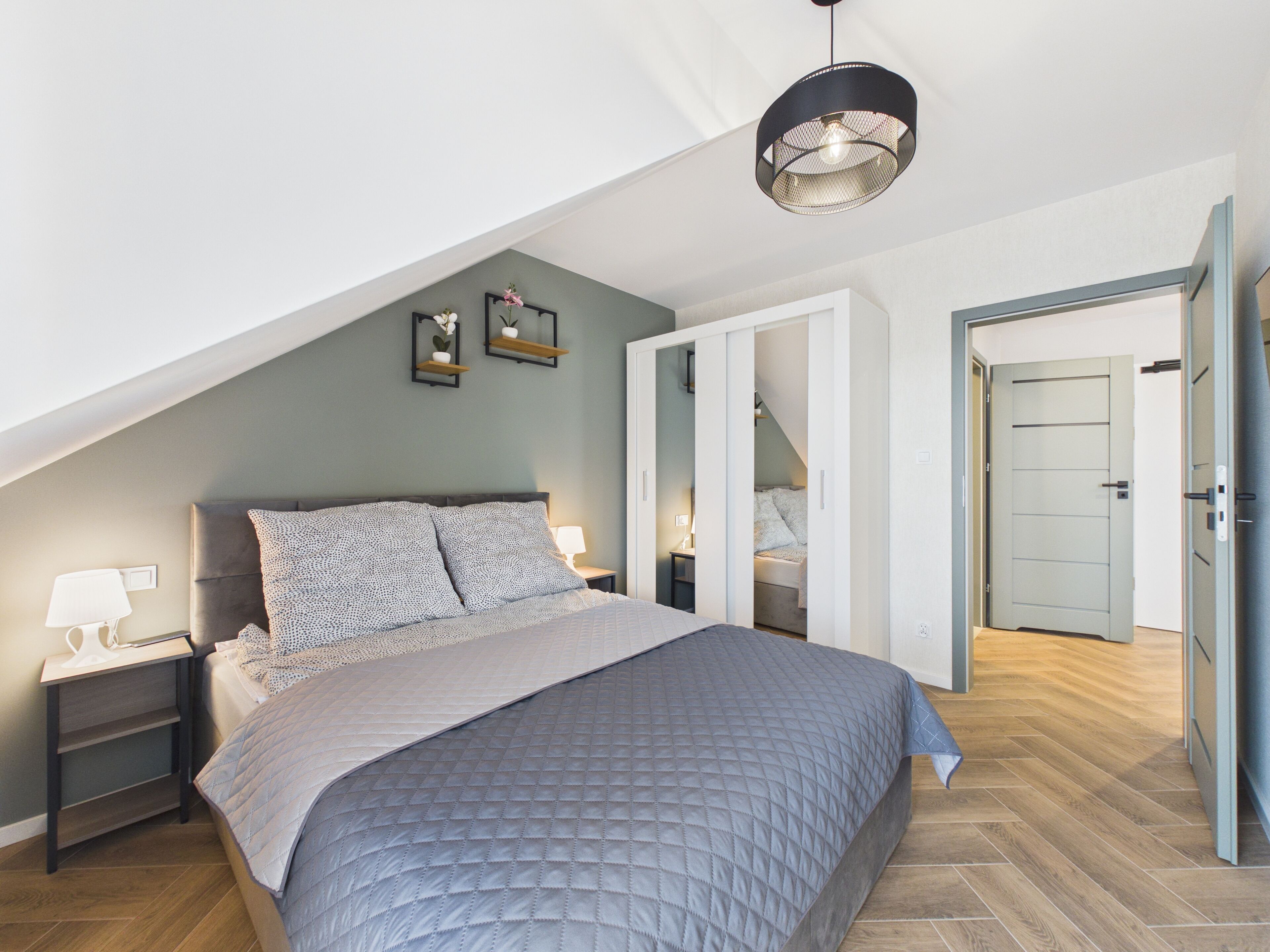 A bedroom with a bed, nightstands, a hanging light fixture, and a wardrobe.