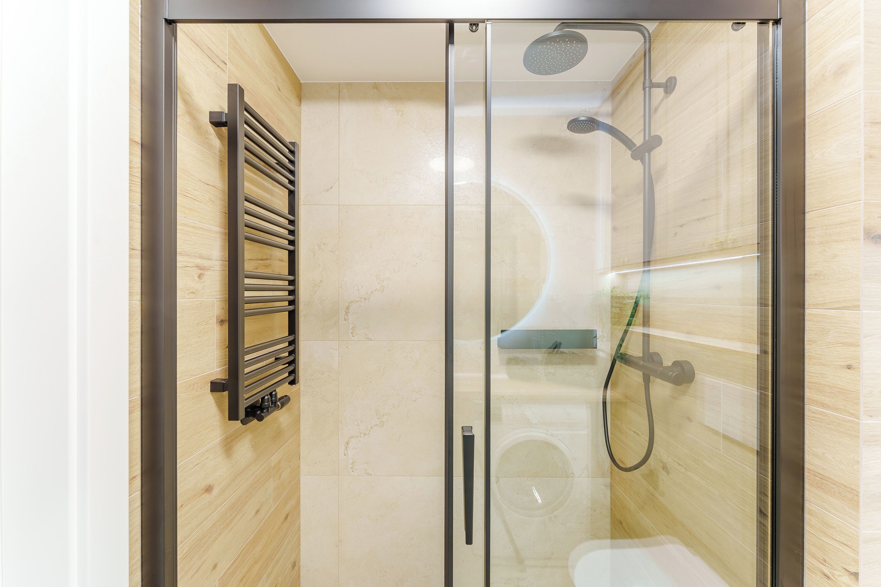 A glass-enclosed shower with a handheld showerhead and a handheld hose.