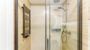 A glass-enclosed shower with a handheld showerhead and a handheld hose.