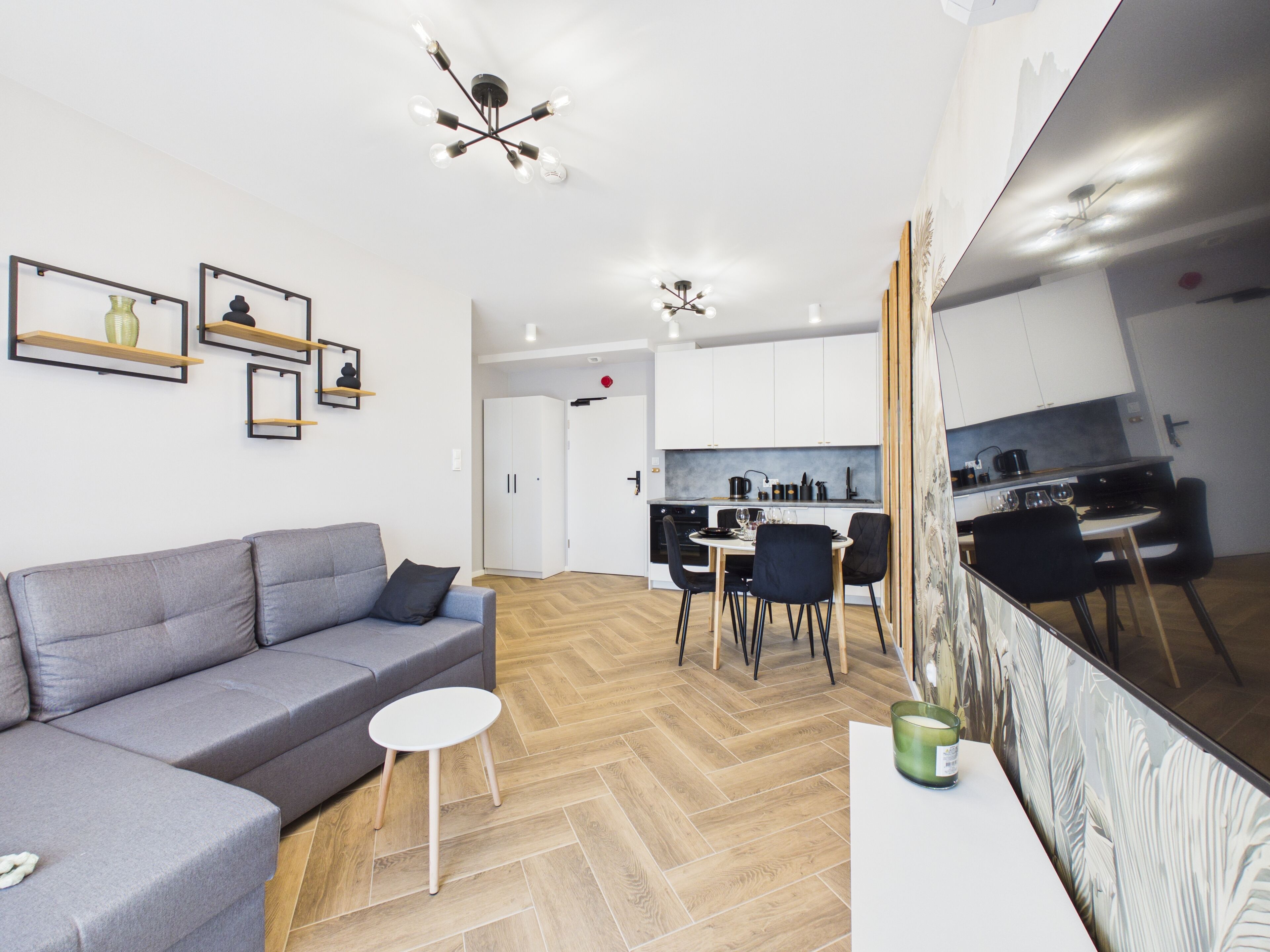 A modern living room with a gray sofa, a small white table, and a herringbone wooden floor.