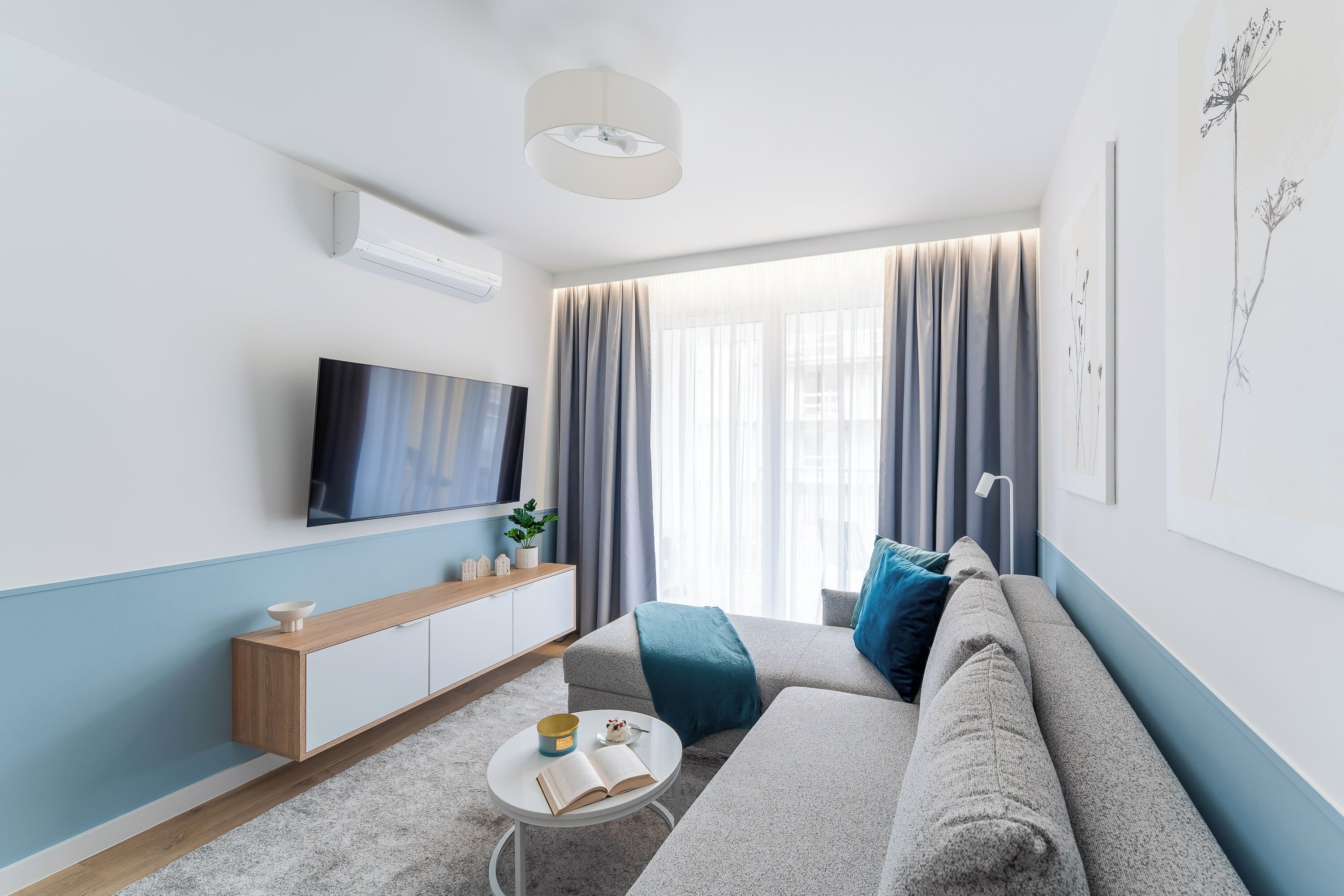 A modern living room with a flat-screen TV, a sofa, a coffee table, and a small side table with a book and a bowl.