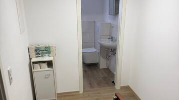 En smal gang med trægulv, en hvid dør og et lille skab med toiletpapir.