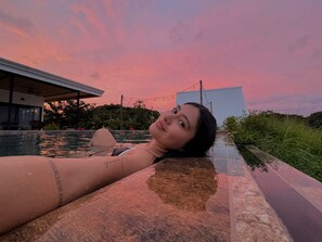 En person slapper af ved en pool med solnedgang i baggrunden.