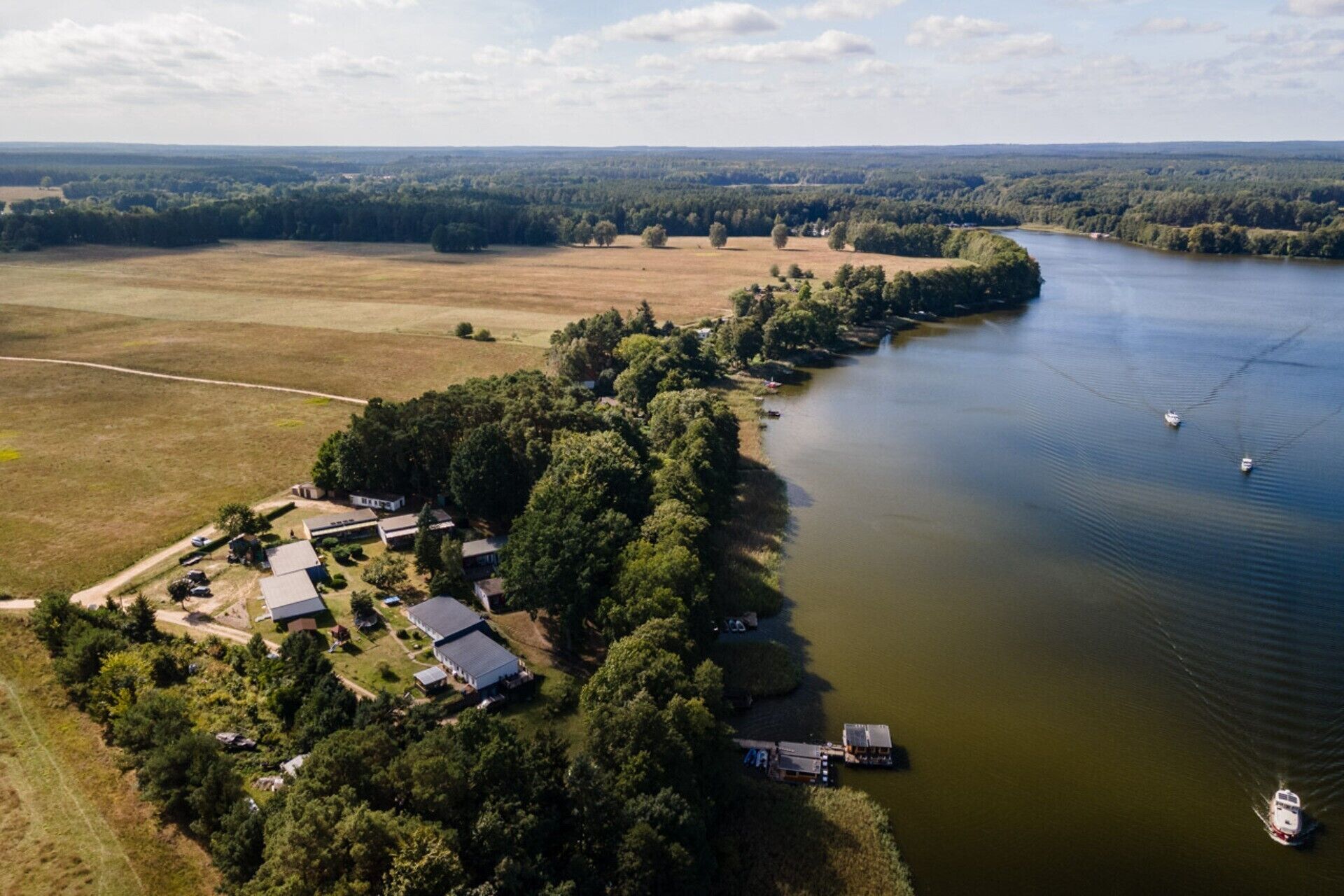 Oversigtsbillede af en ejendom ved en sø med flere bygninger, en anløbsbro og en båd.