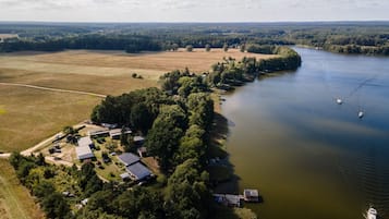 Oversigtsbillede af en ejendom ved en sø med flere bygninger, en anløbsbro og en båd.