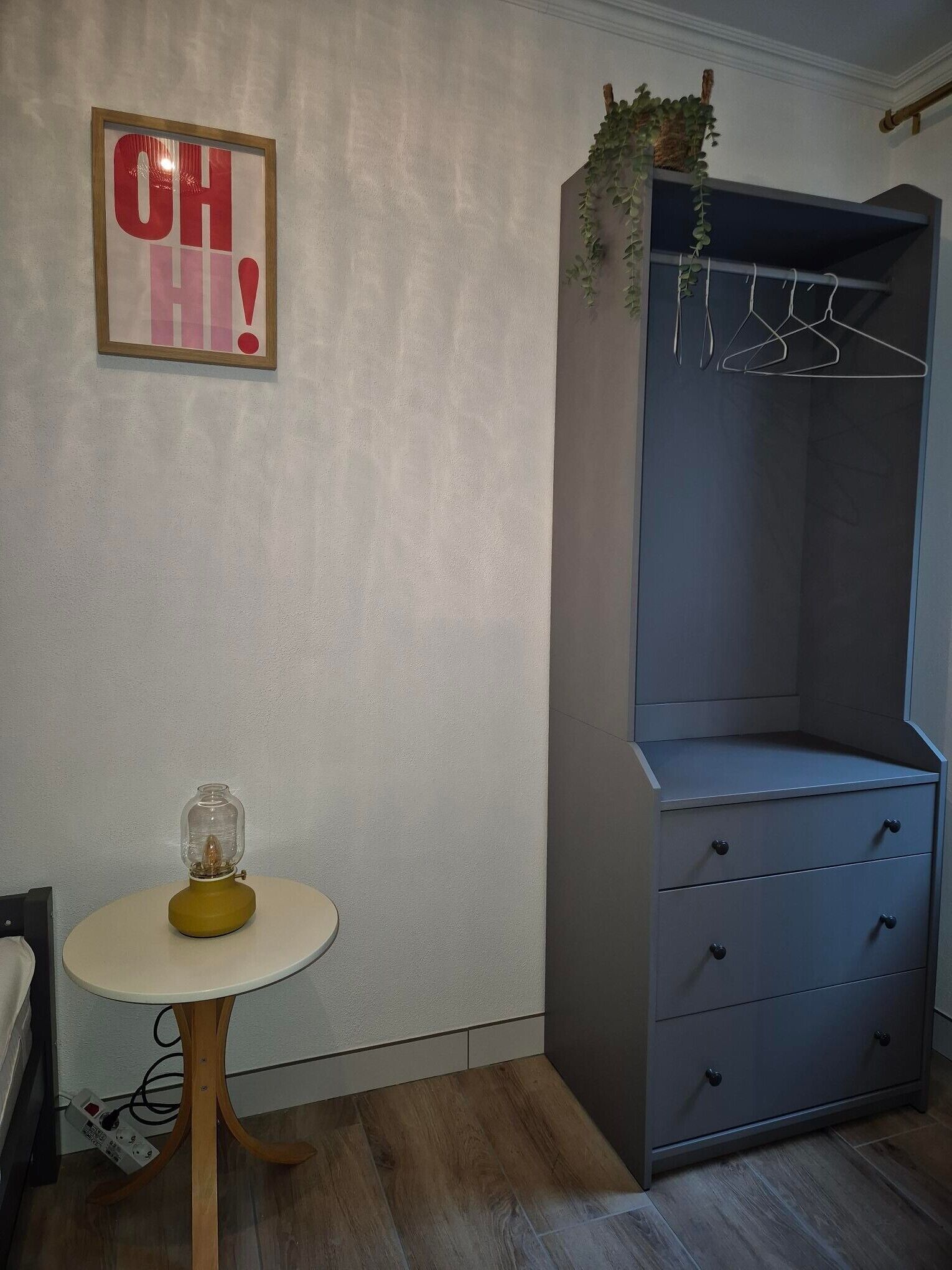 A room with a grey wardrobe, a small round table with a lamp, and a wall-mounted sign.