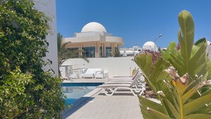 A pool area with lounge chairs, a large building with a dome, and a pathway lined with plants. - Stunning home overlooking the ocean and the golf course (Djerba Midun)