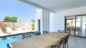A modern dining area with a large table and chairs, a pool, and a view of the outdoors. - Stunning home overlooking the ocean and the golf course (Djerba Midun)