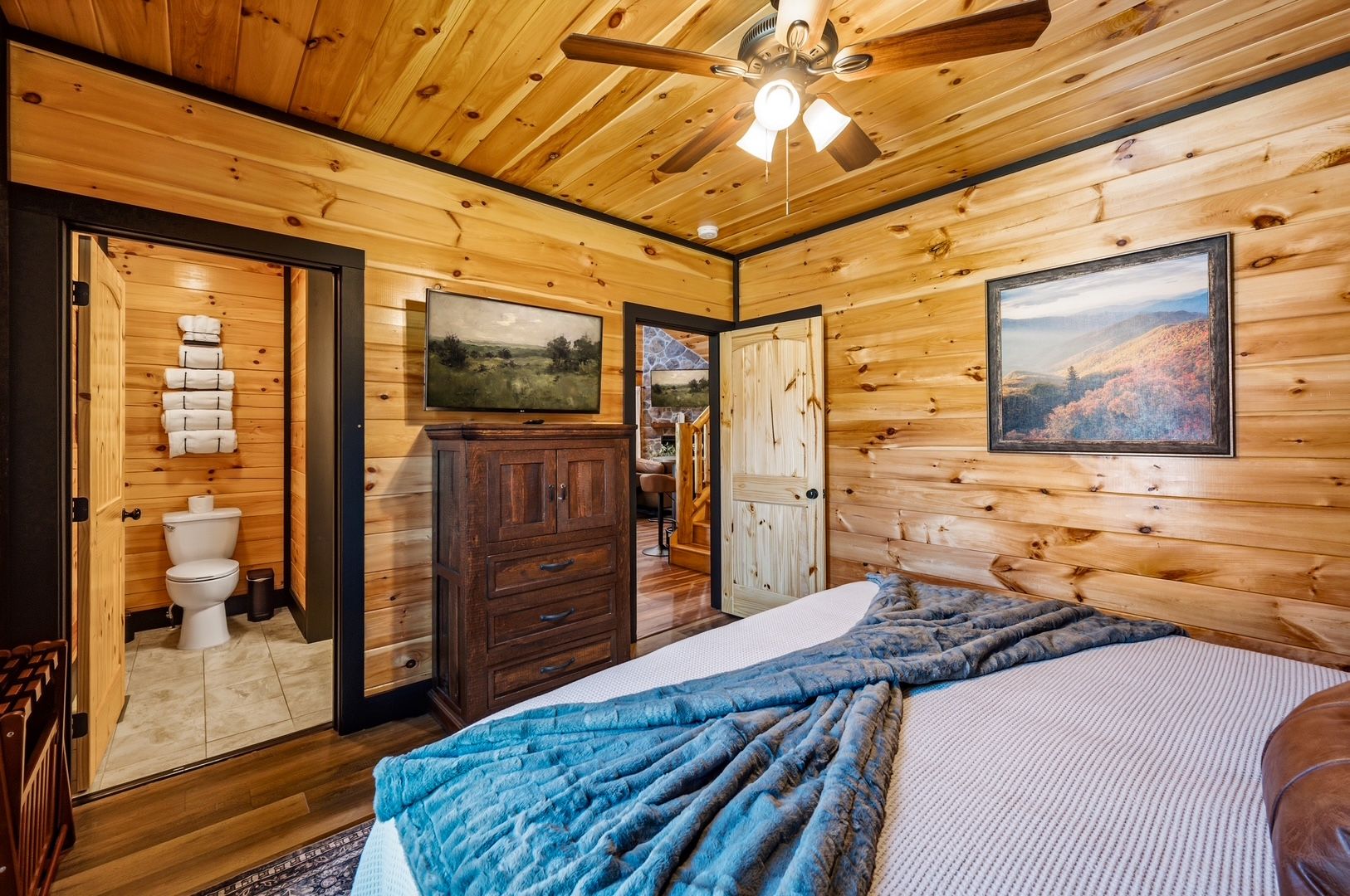 Interior de una cabaña de madera con una cama, un televisor y un baño completo con inodoro y toallas.