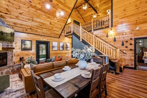 A wooden interior with a dining area, a staircase, and a fireplace. - Hidden Room/Hot tub/Glow in the dark Pool/ Game Room/ Sleeps 12 (Pigeon Forge)