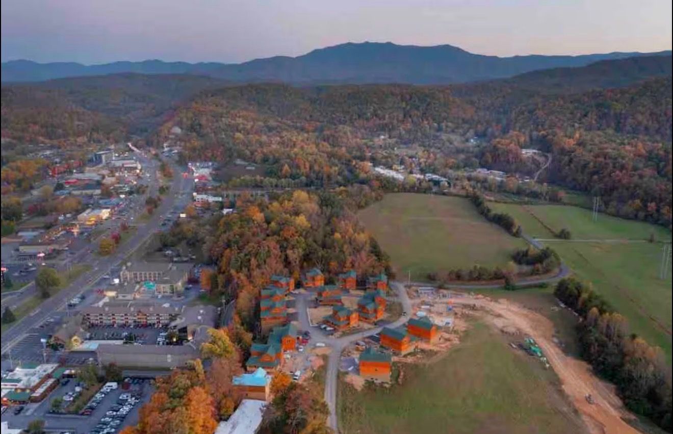 An aerial view of a town with a mix of residential and commercial buildings, surrounded by forested hills.