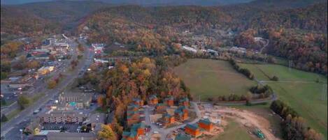 An aerial view of a town with a mix of residential and commercial buildings, surrounded by forested hills.