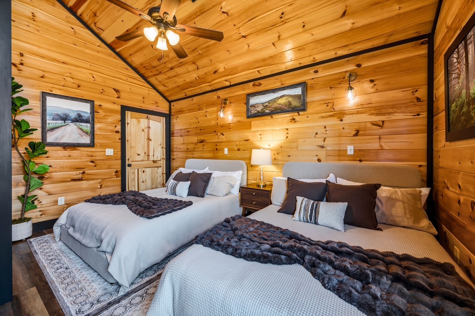 A cozy wooden cabin bedroom with two beds, a ceiling fan, and framed pictures on the walls.